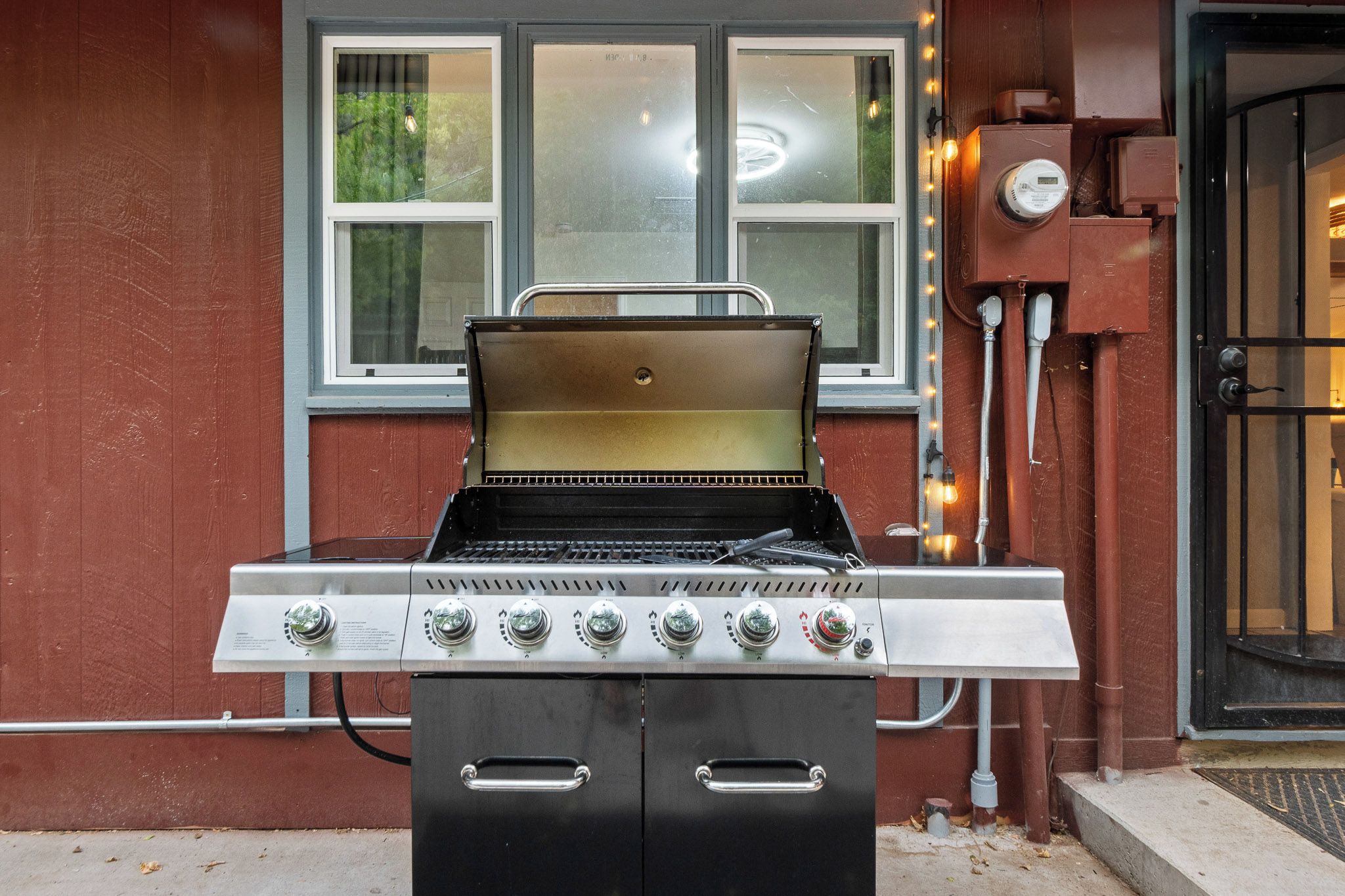 Ein Grill mit digitalem Thermometer vor einer roten Gebäudefassade mit Fenstern und einer Tür.