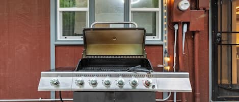 Ein Grill mit digitalem Thermometer vor einer roten Gebäudefassade mit Fenstern und einer Tür.