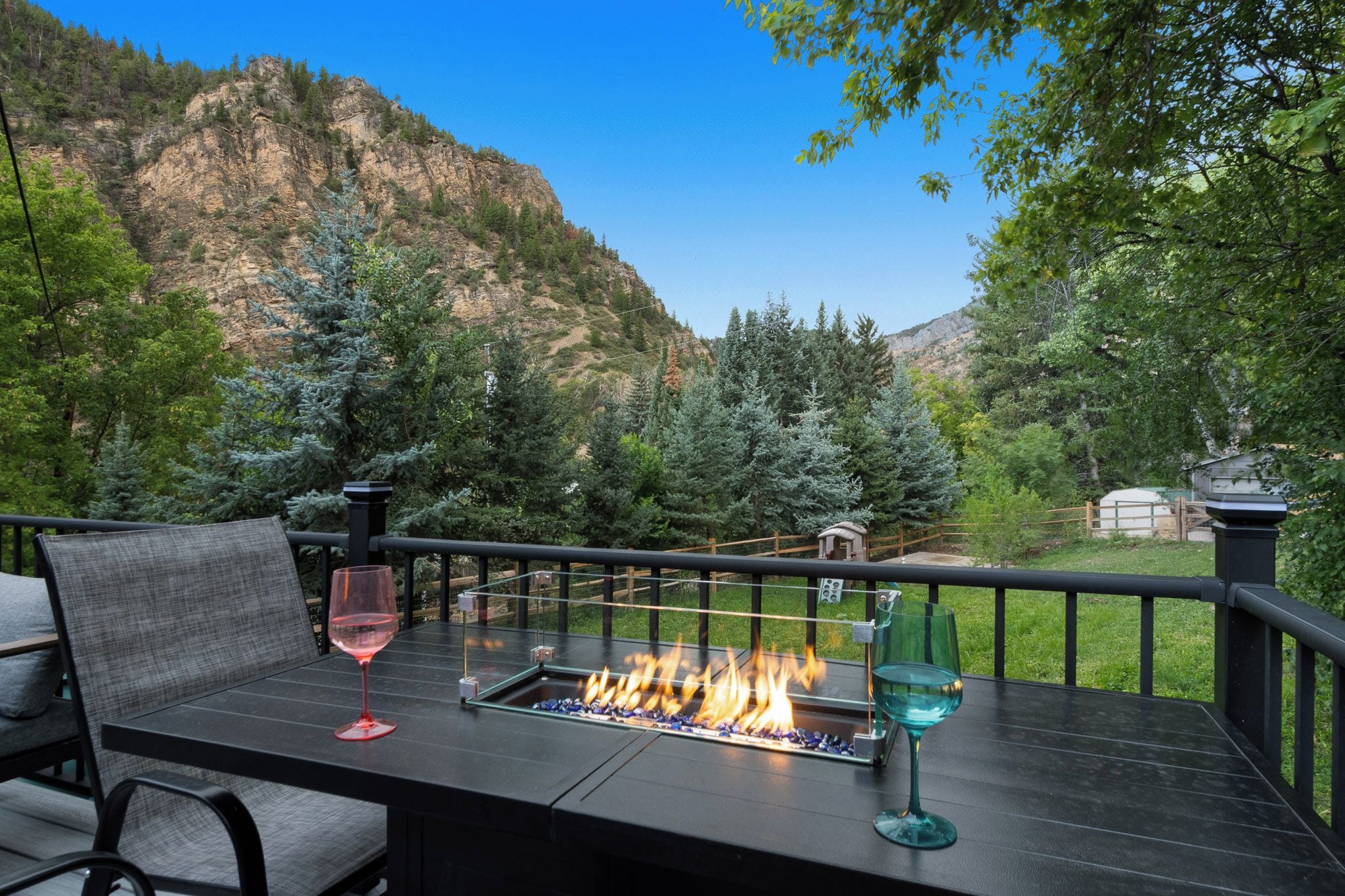An outdoor seating area with a fire feature, a glass table, and a view of a mountainous landscape.