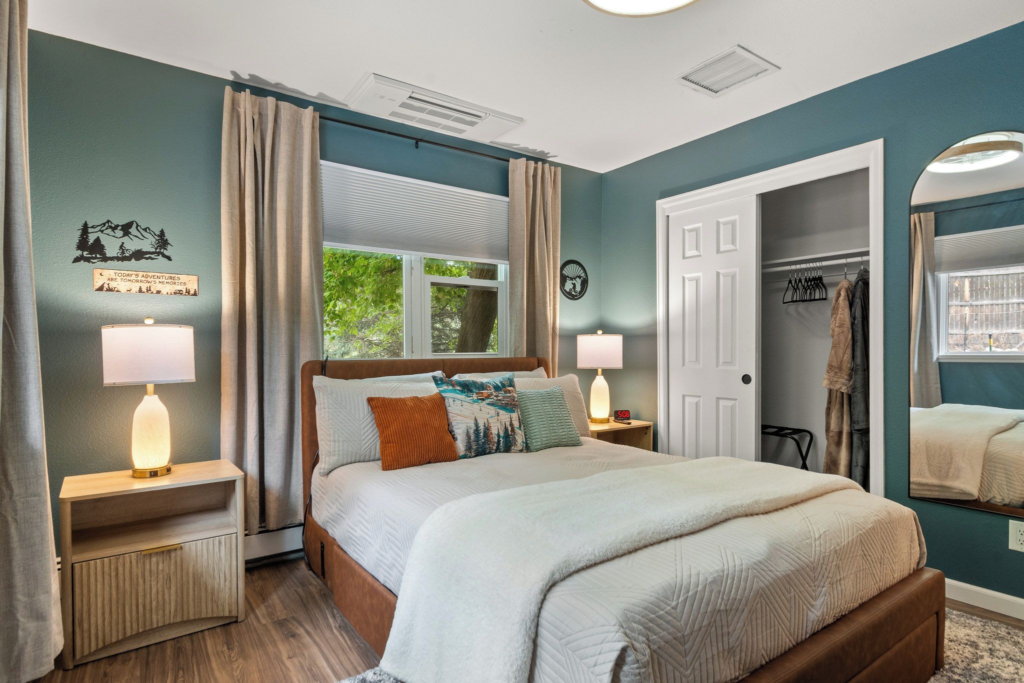 A bedroom with a bed, two bedside tables, a window with curtains, a door, and a coat rack.