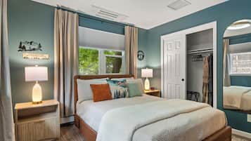 A bedroom with a bed, two bedside tables, a window with curtains, a door, and a coat rack.