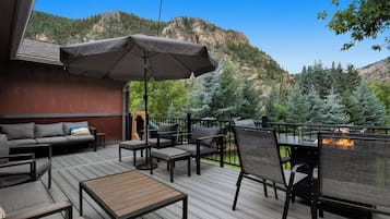 An outdoor deck with a sofa, chairs, and a table, overlooking a mountainous landscape.