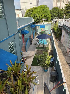 Une cour intérieure d’une résidence, avec une piscine, des plantes en pot et un parasol bleu.