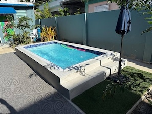 A rectangular swimming pool with a tiled edge, surrounded by a concrete deck and a small grassy area. - Lovely 1 Bedroom Apartment With Private Terrace (San Juan)
