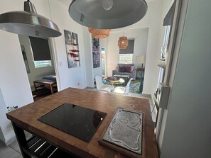 A modern kitchen with a central island, pendant lighting, and a view into the living area. - Lovely 1 Bedroom Apartment With Private Terrace (San Juan)