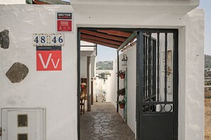 A narrow alleyway with a white building, a black gate, and a sign indicating a sector alarm. - Vacation Home 'Gloria' with Mountain Views, Shared Terrace & Wi-Fi (Arucas)