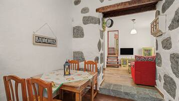 Ein Essbereich mit Tisch und Stühlen, eine Treppe, die in ein Wohnzimmer mit einem roten Sofa führt, und ein Schild mit der Aufschrift 'BIENVENIDOS' an der Wand.