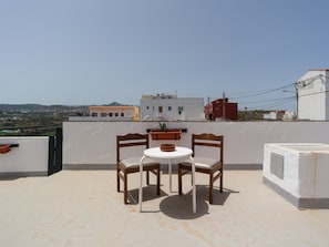 Terraço no telhado com duas cadeiras de madeira, uma mesa pequena e um vaso com planta.