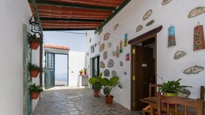 A narrow stone-paved corridor with a wooden bench and potted plants, leading to a door with a stone wall adorned with various decorations. - Vacation Home 'Gloria' with Mountain Views, Shared Terrace & Wi-Fi (Arucas)