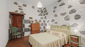 Een slaapkamer met een stenen muur, houten meubels, een bed met bloemenbedekking en een hanglamp.