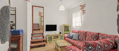 A room with a red patterned sofa, a wooden staircase, a television, and a green cabinet.