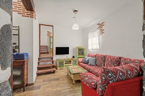 Una habitación con un sofá rojo estampado, una escalera de madera, un televisor y un armario verde.