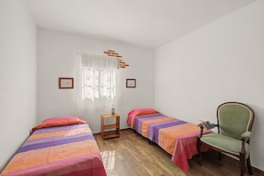 A small, simple room with two single beds, a chair, and a small table.