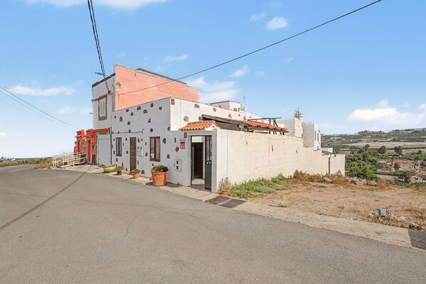 A small, single-story building with a flat roof, a door, and a window. There are potted plants outside.