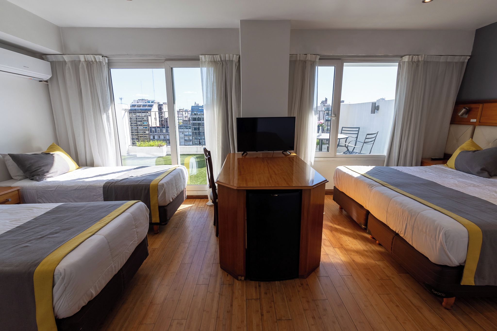 Hotellihuone, jossa on kaksi sänkyä, televisio ja parveke, jolta on näkymä kaupunkiin.