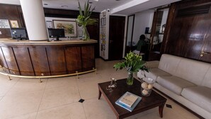 A reception area with a curved wooden desk, a sofa, and a coffee table with a book and decorative items. - AURA HOTEL RECOLETA (Buenos Aires)