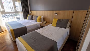 Camera d'albergo con due letti, una testiera in legno, un comodino con il telefono e una finestra vista edifici.