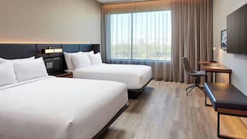 Habitación de hotel con dos camas, un escritorio, una silla y un ventanal con cortinas.