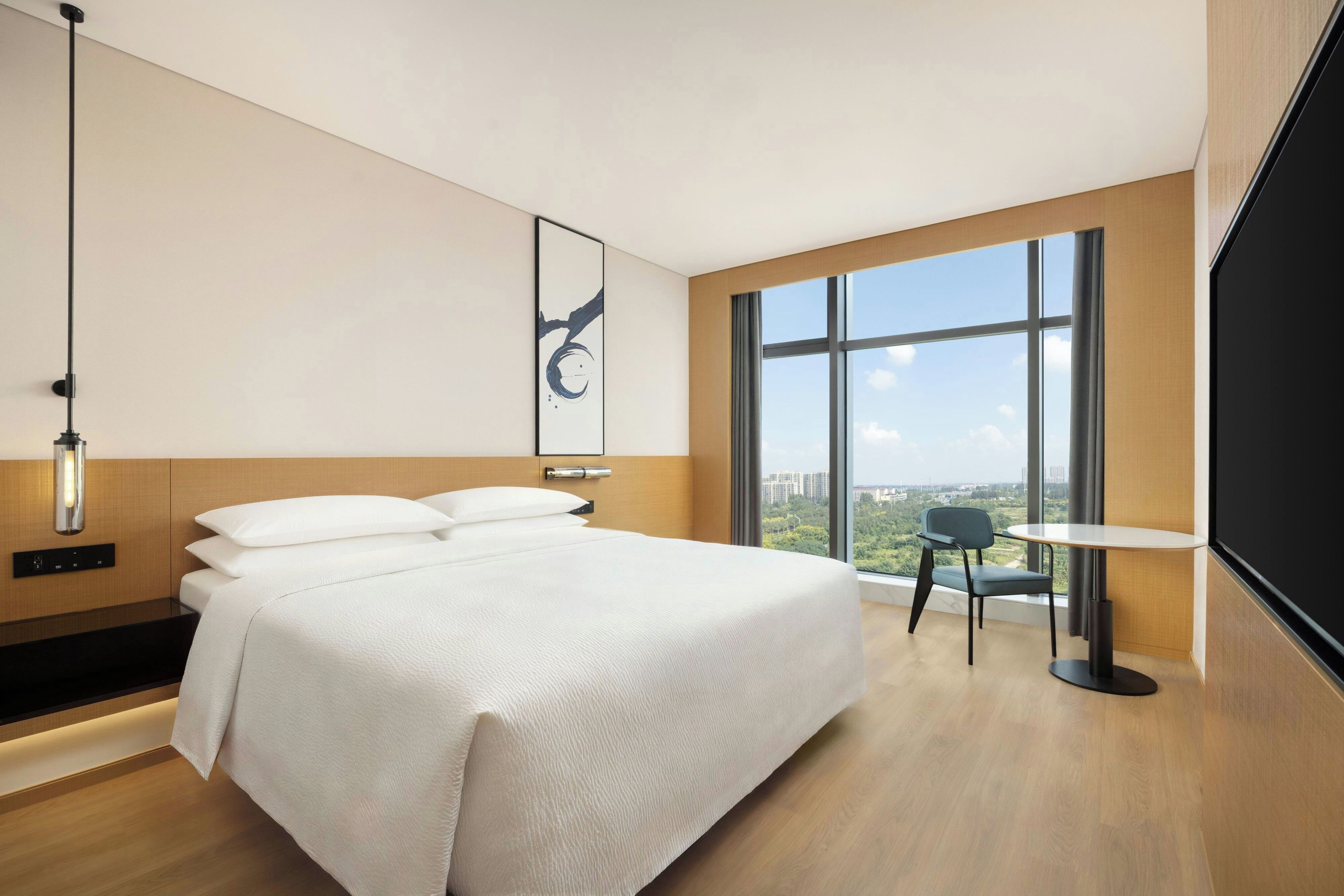 A modern hotel room with a large bed, a desk, and a view of the city.