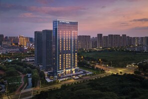 Un hotel moderno de rascacielos con fachada de vidrio, rodeado por un parque cuidado y una calle concurrida.