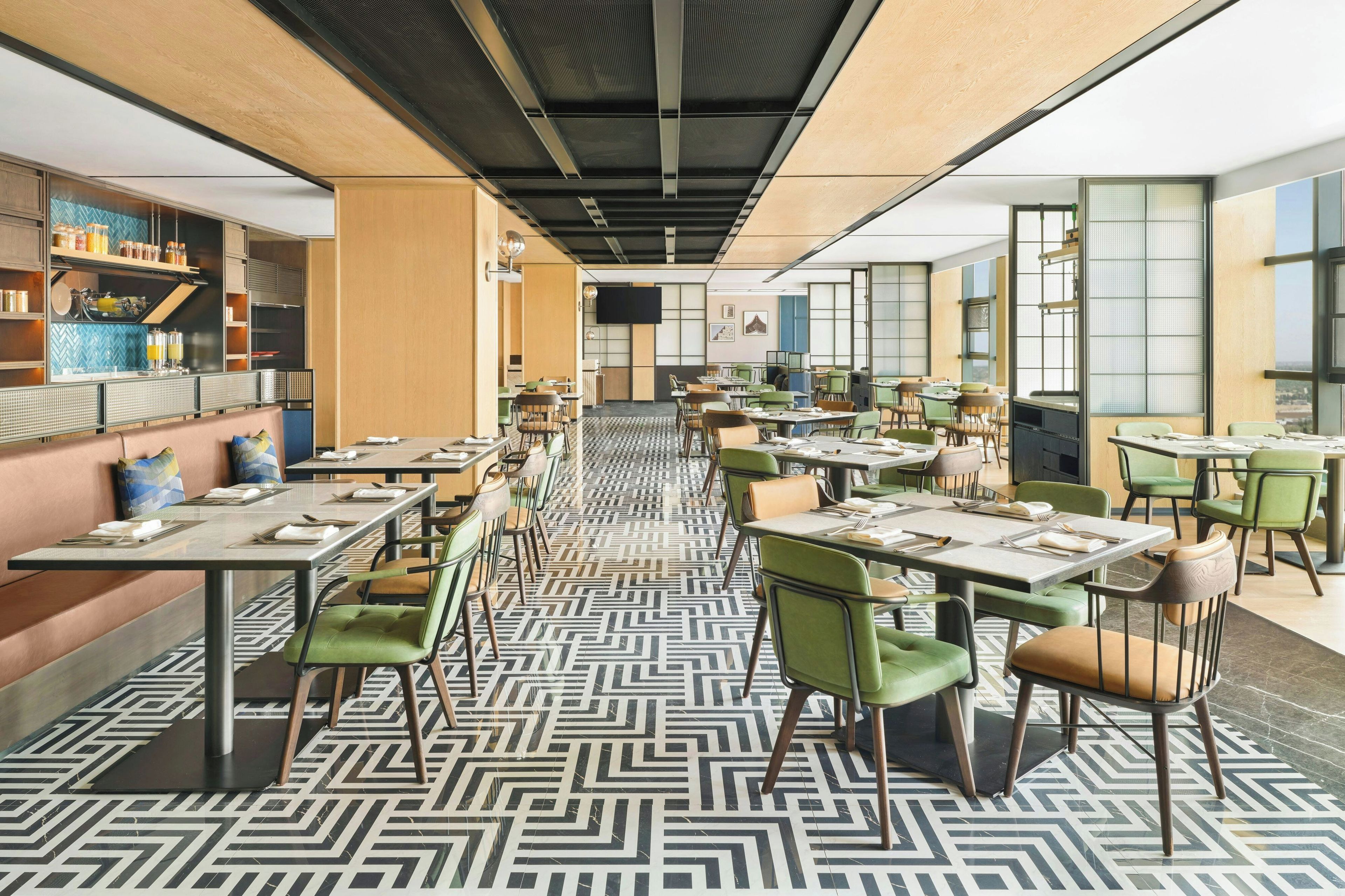 A modern dining area with multiple tables and chairs, a patterned floor, and a kitchen area with shelves and appliances.