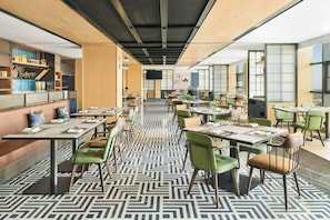 A modern dining area with multiple tables and chairs, a patterned floor, and a kitchen area with shelves and appliances.