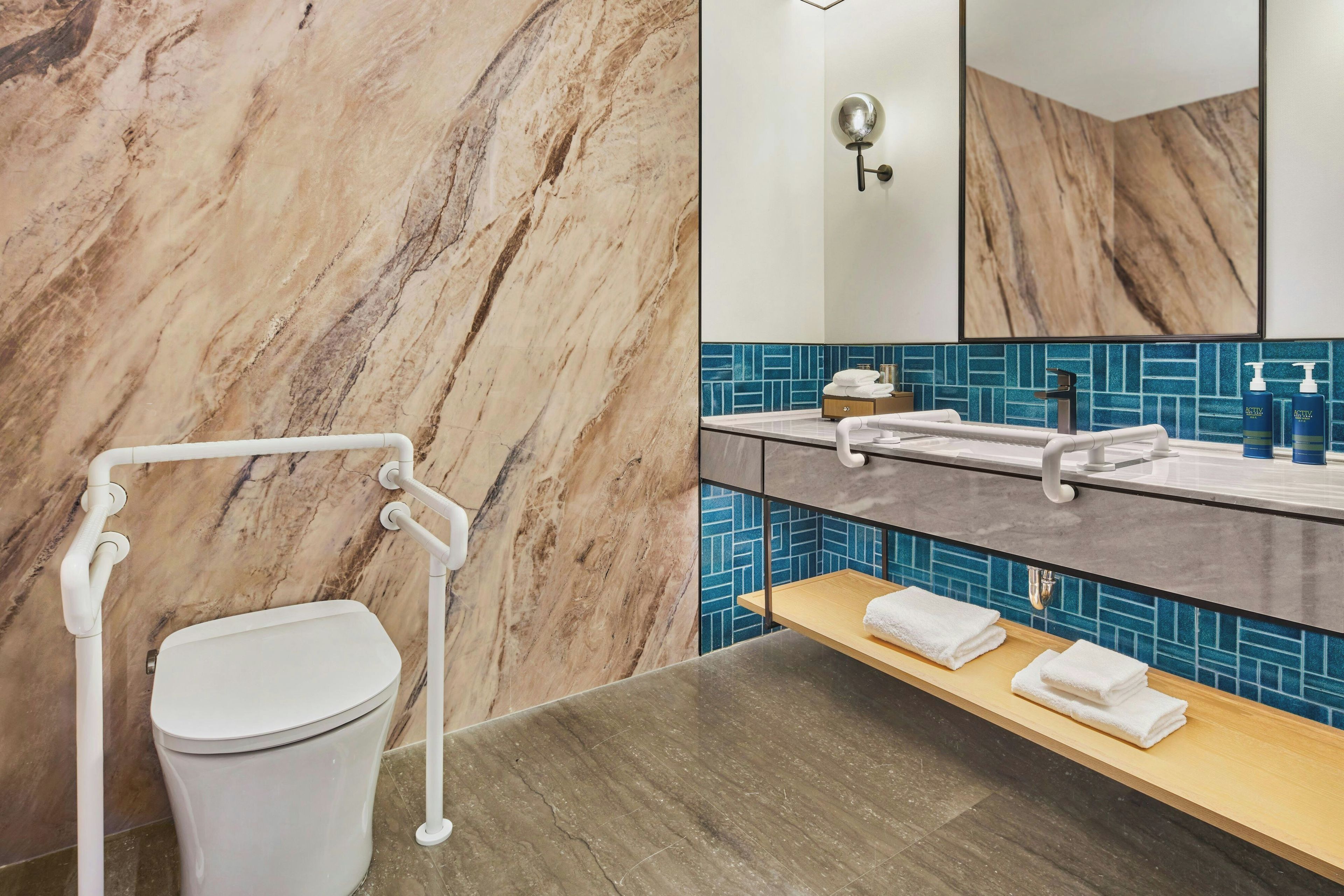 A bathroom with a marble wall, a white toilet, a sink with a blue tiled backsplash, and a mirror.