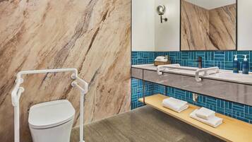 A bathroom with a marble wall, a white toilet, a sink with a blue tiled backsplash, and a mirror.