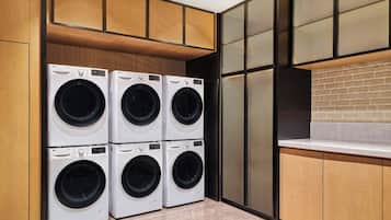 Un cuarto de lavandería con cuatro lavadoras LG ThinQ, armarios de madera, piso de baldosas y pared de ladrillo.