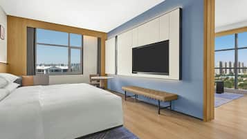 A modern hotel room with a large bed, a small round table, a bench, and a TV mounted on the wall.
