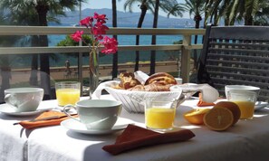 A breakfast table with croissants, orange juice, and a vase of flowers. - LUXURY BEACHFRONT APARTMENT WITH CROISETTE & SEA VIEWS (Cannes)