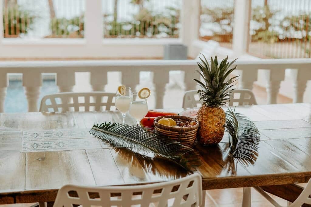 Et træbord med en ananas, en kurv med frugt og et glas drik.
