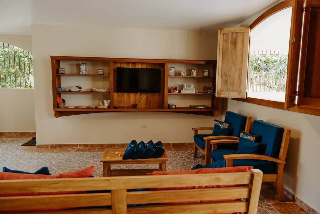 A living room with a wooden TV stand, blue cushioned chairs, and a wooden bench.