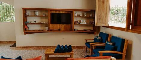A living room with a wooden TV stand, blue cushioned chairs, and a wooden bench.