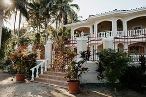 A two-story house with a white exterior, a balcony with a red railing, and a staircase leading to the entrance. - Wiona of Villa Paraiso | Beachfront Villa & Pool (Bocas del Toro Province)