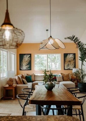A dining area with a wooden table and chairs, a hanging light fixture, and a sofa with cushions. - Wiona of Villa Paraiso | Beachfront Villa & Pool (Bocas del Toro Province)