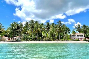 A beachfront property with a sandy beach, palm trees, and a clear blue sky. - Las Casitas of Villa Paraiso | Beachfront & Pool (Bocas del Toro Province)