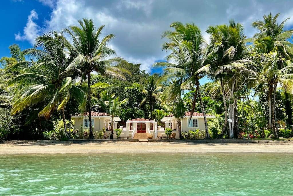 A beachfront property with a central building, palm trees, and clear water.