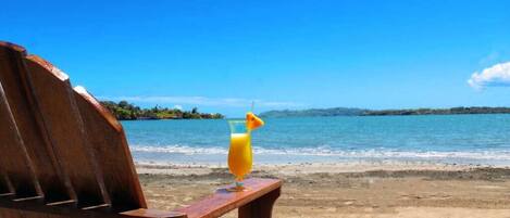A wooden chair with a glass of orange juice on a beach.
