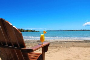 Ein Holzstuhl mit einem Glas Orangensaft am Strand.