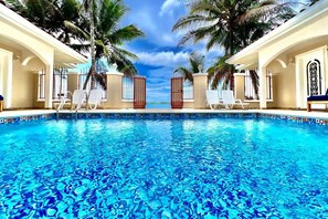 Une piscine à l’eau d’un bleu cristallin, entourée de chaises longues blanches et de palmiers.