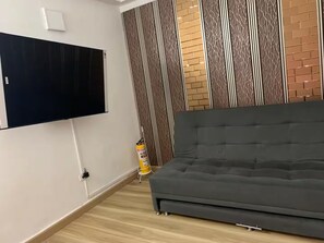 A room with a grey sofa, a mounted TV, a patterned wall, and a fire extinguisher. - Moon House: Modern, Comfortable, and Elegant. (Cali)