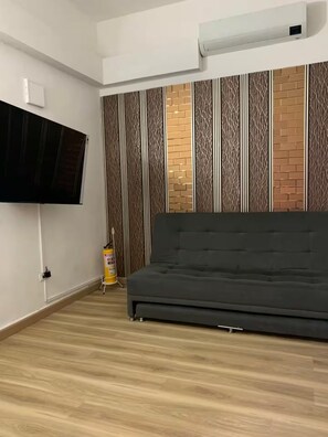 A room with a large flat-screen TV mounted on the wall, a grey sofa, a patterned wall, and a fire extinguisher. - Moon House: Modern, Comfortable, and Elegant. (Cali)