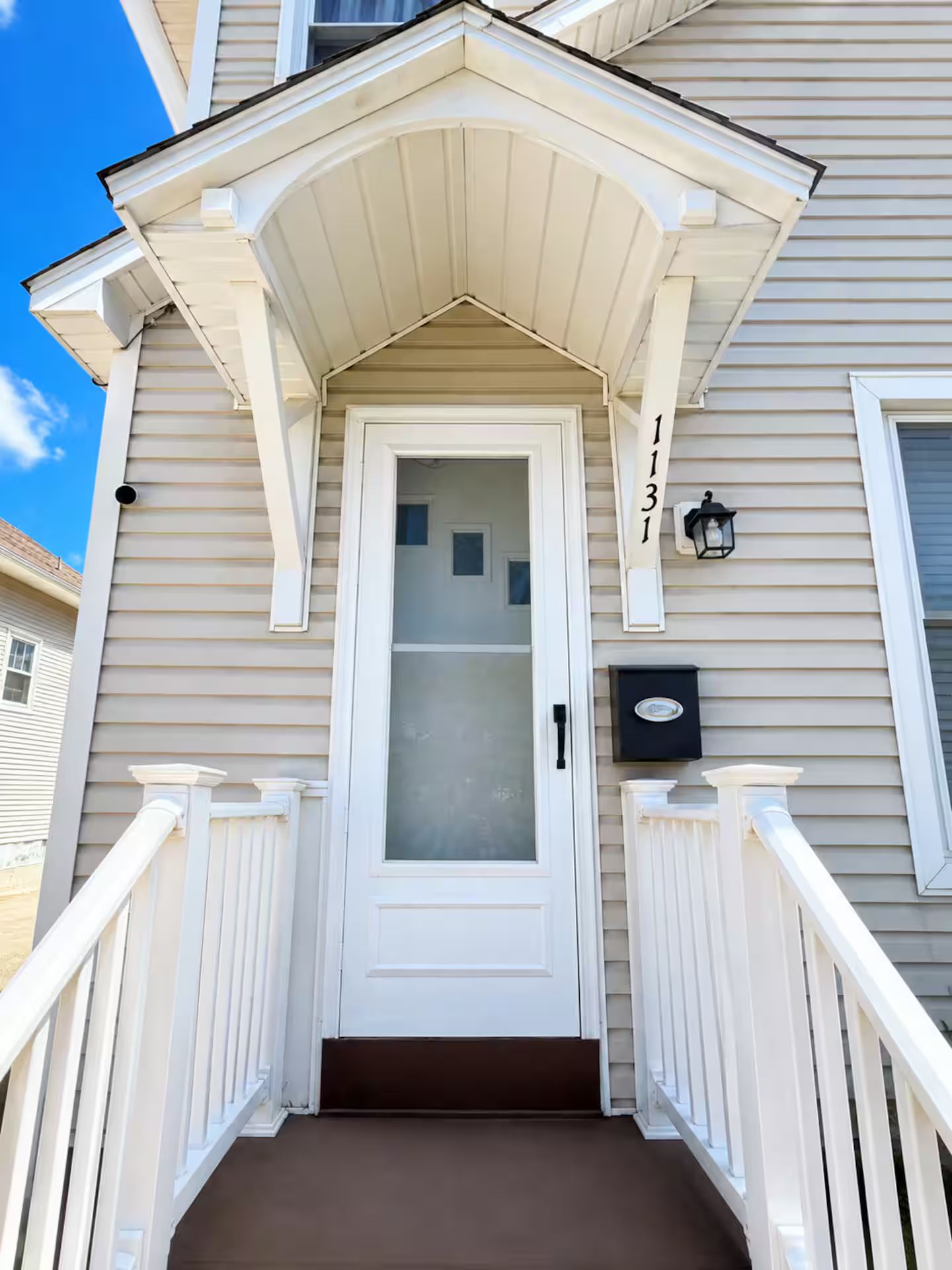 A house with a white front door, a mailbox, and a small porch with white railings.