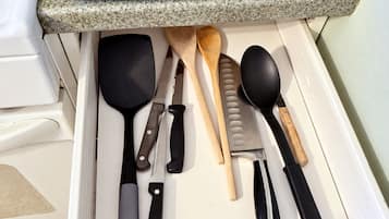 Un cajón de cocina con varios utensilios, incluyendo una toalla azul, una espátula, un cuchillo, una cuchara de madera y una cuchara para servir.