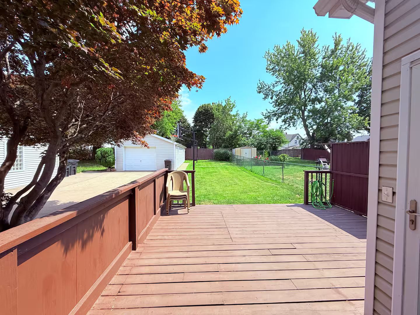 A wooden deck with a view of a backyard, a white garage, and a red fence.