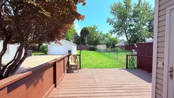 A wooden deck with a view of a backyard, a white garage, and a red fence.