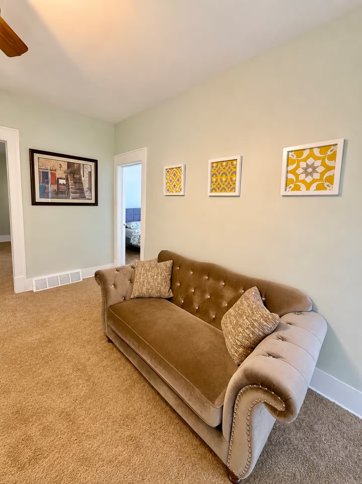 A living room with a brown sofa, a framed picture, and a door leading to another room.