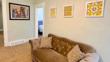 A living room with a brown sofa, a framed picture, and a door leading to another room.