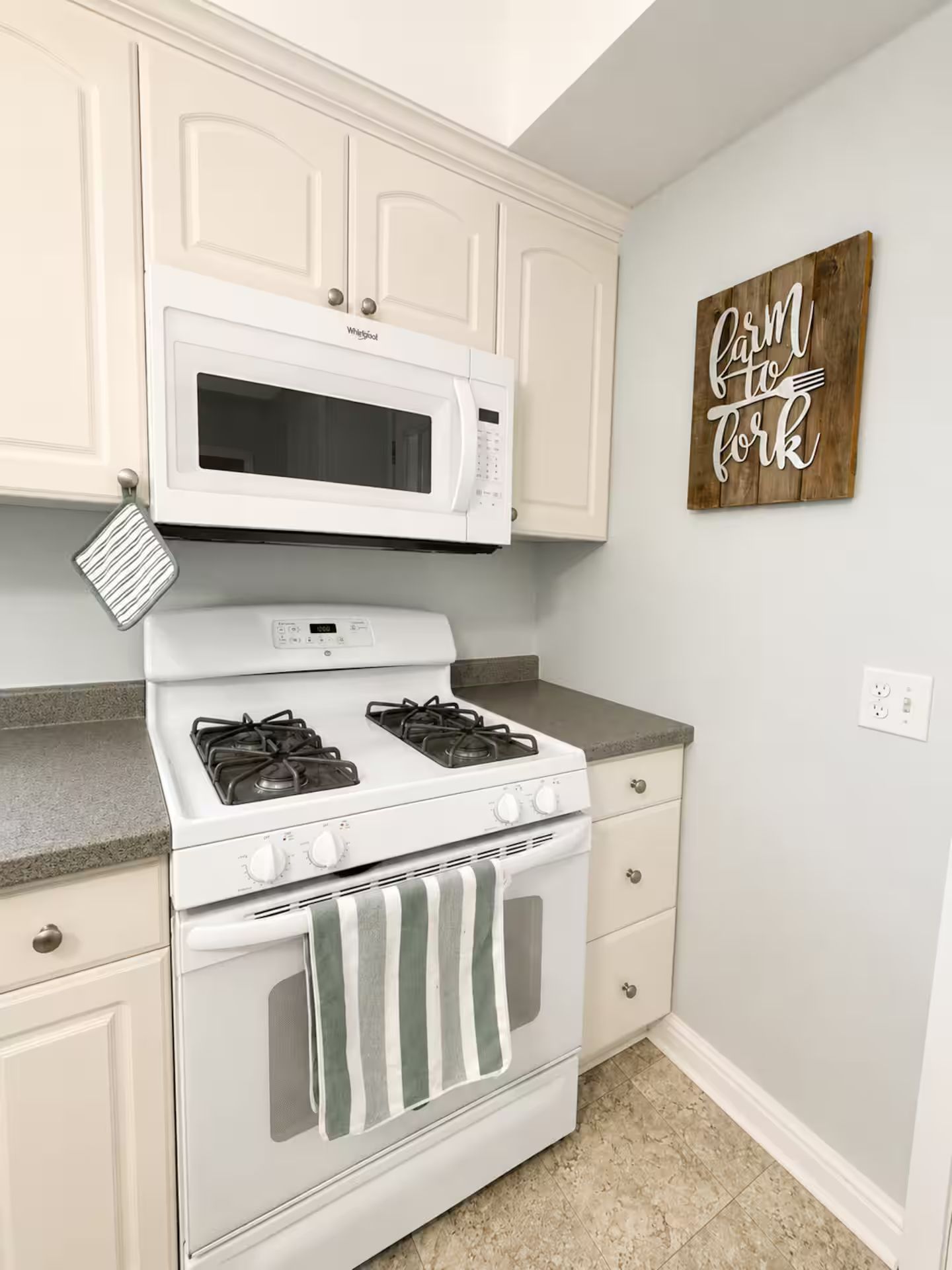 A kitchen with white cabinetry, a white microwave, a stove with four burners, and a wooden sign on the wall.